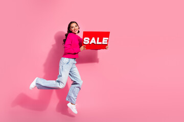 Young chic woman jumps with a bright sale sign against pink background promoting shopping and...