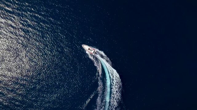 Overhead tracking view of a RIB motorboat driving in circles with speed over blue ocean