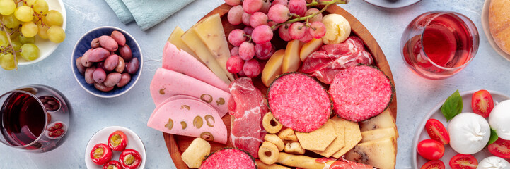 Italian Antipasti panorama. Charcuterie platter with cheese and other snacks, with wine, olives, fruit, etc, overhead flat lay panoramic shot