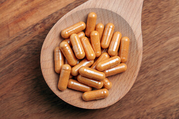 Top view of golden plant based pills inside a carved wooden spoon on kitchen surface