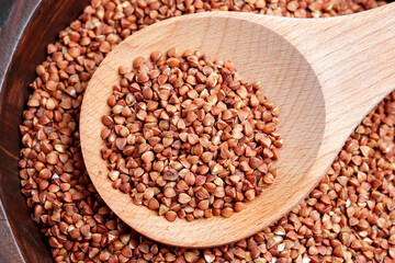 Obraz premium Raw buckwheat groats in a wooden spoon on a bowl filled with dry grains. Healthy cereal ingredient. Clean eating concept. Top view