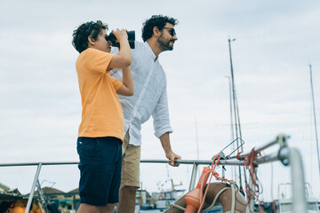 Father and son looking through binoculars on a boat, curiosity and exploration
