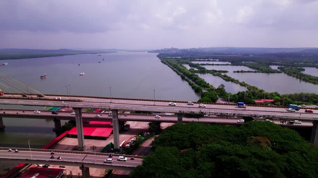 Reveal shot of atal setu bridge with moving vehicles, greenery and Mandovi River at goa, india. day time, push back with pan shot, drone shot, 4k.