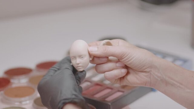 Closeup of artist assembling silicone doll head with both hands, showing delicate handling and detailed work in handcrafted miniature figure production