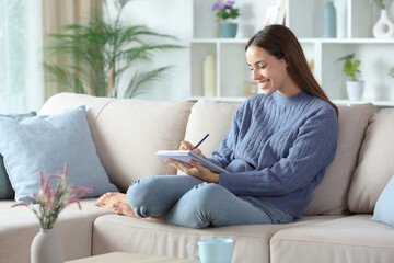 Happy woman in blue taking notes on notebook at home