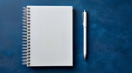 Blank white spiral notepad and white pen resting on a deep textured blue background, concept for office supplies, memo taking and business planning
