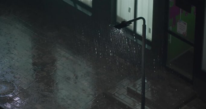 Heavy rain falling on city street at night, illuminated by street light with visible raindrops and wet pavement
