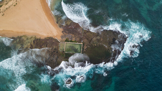 Aerial view of crashing waves meeting the shore at North Narrabeen rock pool, creating a mesmerizing dance of turquoise and white foam, Sydney, New South Wales, Australia.