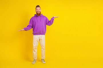 Happy young man in purple hoodie and beige pants poses with open arms against a yellow background