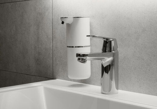 New 2026 trend Cloud Dancer color. Modern bathroom hygiene setup in a minimalist interior, featuring a chrome faucet and a white automatic, touchless soap dispenser in a ceramic sink.
