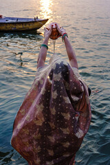 India. Uttar Pradesh state. Varanasi (Benares). A Hindu woman, dressed in a richly adorned sari, performs the Surya Arghya ritual (offering of water to the Sun) in the sacred Ganges River at sunset