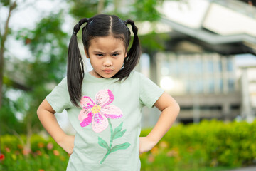 Cute little girl at camera with angry expression. she is arms akimbo while standing against. Kid...