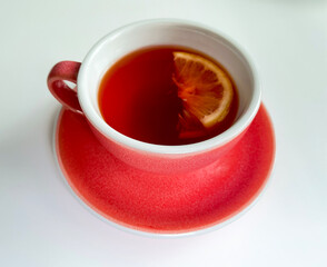 Coral-colored ceramic cup with lemon tea on a light background.