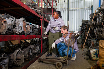 Workers working in a auto parts warehouse, examining salvaged parts. The warehouse is well-organized with multiple shelves