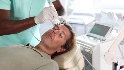 European man is lying on couch during facial skin care procedure. Dermatologist cosmetologist using nozzle of beauty machine ultrasonic import promotes deep penetration of therapeutic cream into skin