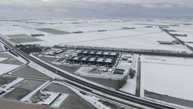 Aerial view of long, dark rectangular buildings contrasting against the bright white snow-covered fields, Datacenter, Noord-Holland, Netherlands.