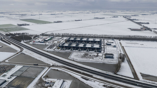 Aerial view of a sprawling data center complex surrounded by snow-dusted fields and waterways under a grey sky, Datacenter, Noord-Holland, Netherlands.
