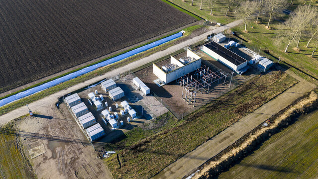 Aerial view of an electrical substation with stark white buildings contrasting against the dark earth and crisp blue canal, Almere, Netherlands.