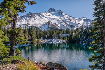 A mountain range is in the background of a lake. The lake is calm and clear, reflecting the snow-capped mountains. The scene is peaceful and serene