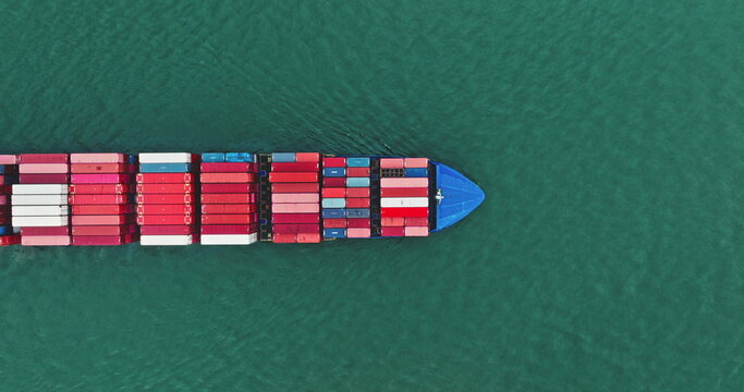 Cargo ship navigating through the open ocean, freight containers stacked on deck, illustrating global logistics, international trade, and marine transportation from a top down aerial perspective