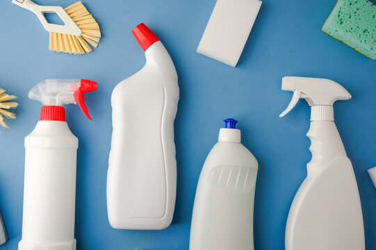 White cleaning bottles and sponges on blue surface, household cleaning supplies