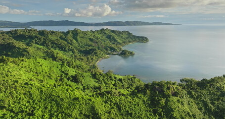 Lush green jungle hills meet the tranquil blue ocean along Vanua Levu Savusavu coastline, under a partly cloudy sky pristine tropical paradise seen from above