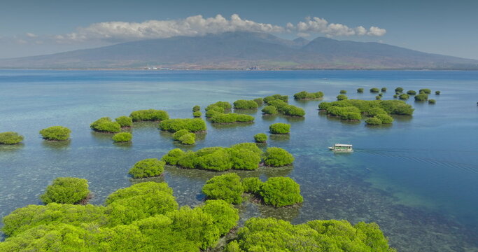 Gili Islands: aerial view small tourist boat sailing clear turquoise sea with green mangrove islands surrounded by shallow coral areas. Lombok mountain range in background. Travel, adventure, explore