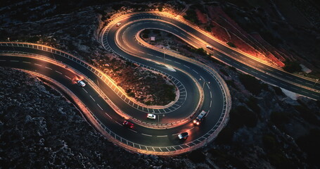 Malta: cars driving on winding night road with orange street lights, creating visually striking scene with illuminated headlights and taillights. Aerial view drone flight , top down