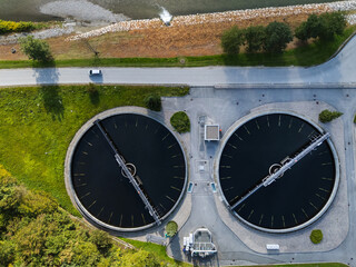 Drone view of a modern wastewater treatment plant displaying circular settling tanks and integrated green landscape for water management.