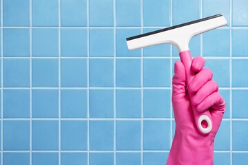 Hand in pink glove against blue tile cleaning with squeegee for streak free bathroom glass.