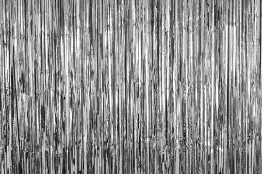 Shiny silver fringe curtain background with vertical metallic strands reflecting light.