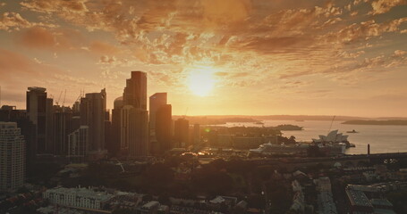 Australia, Sydney: Bright warm glow orange sunset over Sydney's modern skyline creates stunning scene of iconic Opera House and Harbour, modern city architecture. Aerial view drone panorama