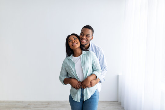 Loving millennial african american couple posing in empty apartment, embracing and looking at copy space, moving in and dreaming, free space. Real estate concept - Powered by Adobe