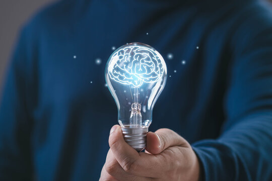 Hand holding glowing light bulb with digital human brain inside, symbol of intelligence, smart thinking, artificial intelligence, innovation knowledge for technology, education business development.