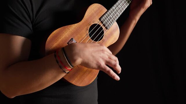 Hands playing a classic brown acoustic ukulele with white wooden strings on a black background as a folk musical instrument ready to play a jazz and rock concert.