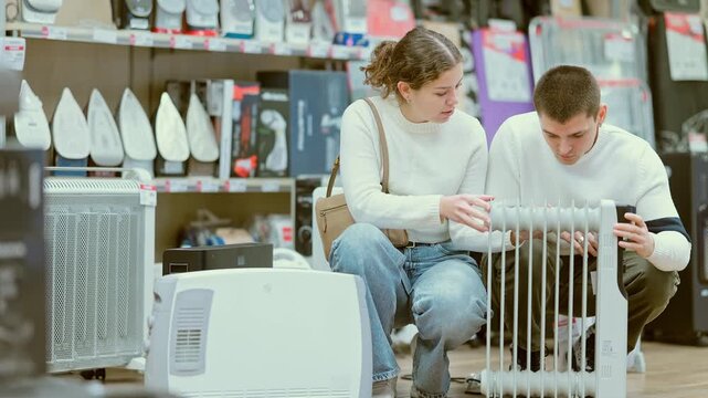  Young couple man and woman choosing electric oil heater in home appliance store