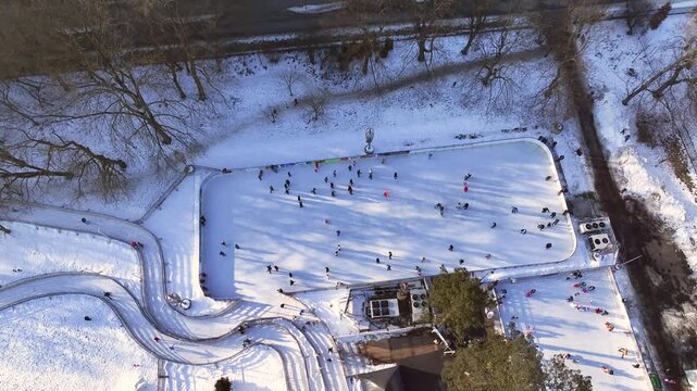 People skate on an outdoor rink surrounded by snow-covered trees and buildings