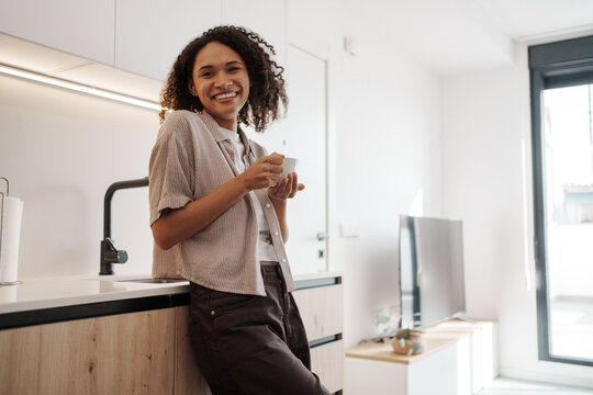 Comfortable Woman Leaning Against Kitchen Table, Laidback Lady Enjoying Coffee In Bright Apartment