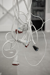 Tightly tangled bundle of white industrial extension cables with red and black connectors hanging in a workspace. Blurred concrete floor and background with copy space