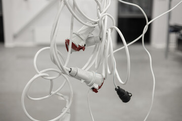Tightly tangled bundle of white industrial extension cables with red and black connectors hanging...