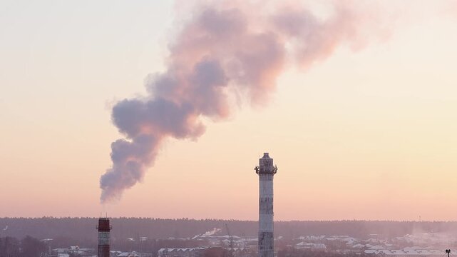 Smoke escapes from an industrial chimney into the atmosphere. A bird's eye view of industrial chimneys on a winter evening during sunset.