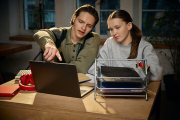 Brother explaining homework to sister during home study. Concept of family mentorship, sibling learning, education support, calm study routine, everyday home schooling.