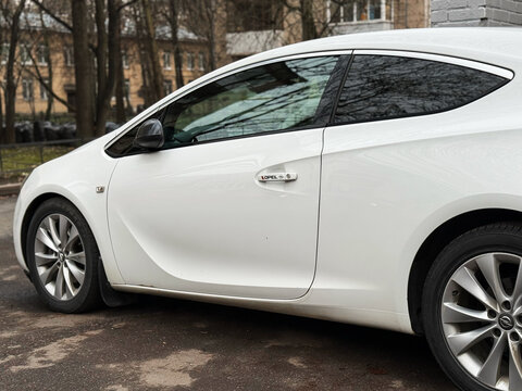White Opel Astra J GTC in the city street. Motor sports car Opel Astra J GTC hot hatch in the city street. Opel Astra GTC OPC hatchback. German sport hatchback.