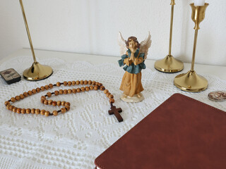 Catholic corner at home. Angel figurine, wooden rosary beads, cross, and prayer book. Faith, symbols, and traditions.