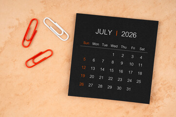 Black calendar sheet for July 2026 with paper clips on paper.