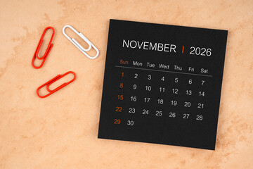 Black calendar sheet for November 2026 with paper clips on paper.