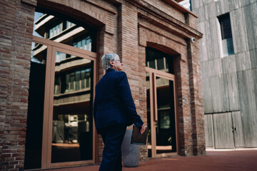 Rear view of senior professional woman walking with digital tablet, showcasing progress, mobility, and confidence in managing tasks with technology on the go.