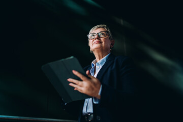 Senior executive woman with tablet looking up with confidence. Visual metaphor for strategic foresight, digital leadership, and readiness for tech-driven business change. © BullRun