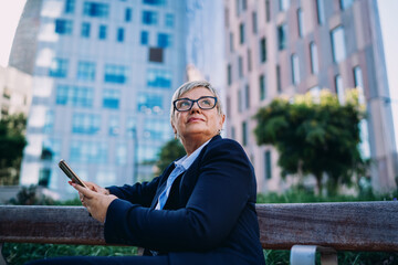 Close-up of senior businesswoman with smartphone in hand, gazing forward confidently, expressing vision, readiness, and digital control in the modern business landscape. © BullRun