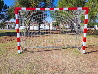 Football goals are positioned in a park surrounded by trees and open space during the day